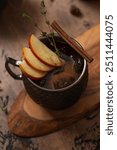 Apple Moscow Mule cocktail in a copper mug on a wooden rustic background. Autumnal Spiced Cider with honey, apple slices, thyme and cinnamon stick as a garnish. Cozy autumn evening. Drink photography