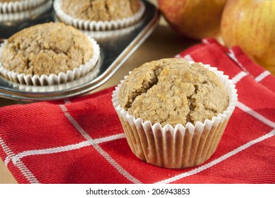 An Apple Oatmeal Muffin With More Muffins In A Tin And Apples In The Background