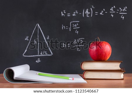 Apple on book and green wooden pen on opened notebook on desk. Pythagorean theorem written by chalk on blackboard. School classroom and education concept. Close up, selective focus