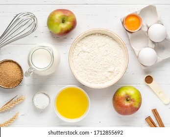 Apple pancakes or apple muffins ingredients top view. Flour, eggs in eggholder, bottle of milk, brown sugar, cinnamon powder, fresh apples, melted butter and baking powder. White wooden background. - Powered by Shutterstock