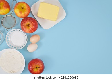 Apple pie baking ingredients with butter, flour, sugar, eggs and fruits on blue background with copy space
