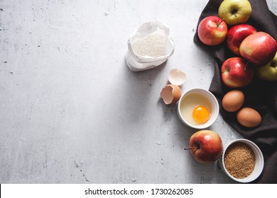 Apple pie ingredients: a bag of flour, eggs, egg with yolk in a bowl, brown sugar, egg shells, dark linen cloth, apples on light grey concrete background. Top view, flatlay, copy space. Recipe Mockup - Powered by Shutterstock