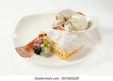 Apple puff pastry strudel with apple filling, served with fresh berries (raspberries and blackberries) and a sprig of mint in a chocolate sauce and a bowl with a scoop of vanilla ice cream, garnished 