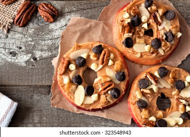 Apple rounds with peanut butter, chocolate chips and nuts, downward view on paper with rustic wood background