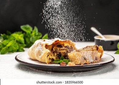 Apple strudel cake with cinnamon, mint and raisins on light background, with sieve sprinkling sugar powder from above. austrian germany food.
