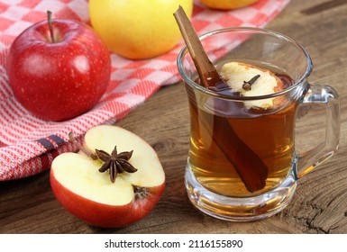 Apple Tea In Glass With Dried Slice Of Apple And Clove On Top. Homemade Tea From Dried Apples And Hot Water. Stick Of Cinnamon In Tea And Half Of Red Apple With Star Anise On Brown Wooden Table. 