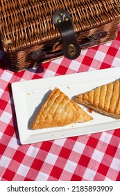 Apple turnover on a white plate, with a wicker picnic basket,  outdoors in sunshine. on a gingham cloth. background - Shutterstock ID 2185893909