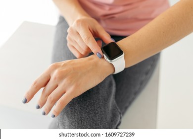 Apple Watch With A White Strap On Her Hand. Girl In A Pink T-shirt And Blue Jeans.