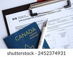 Application for permanent resident card on table with pen and canadian passport close up