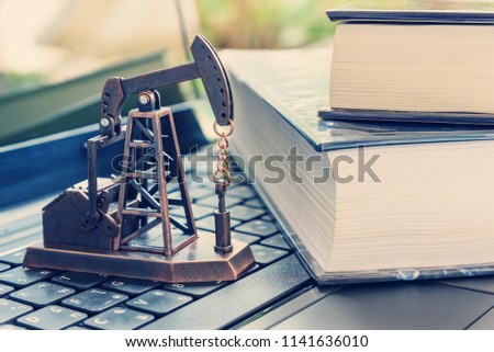 Applied petrochemical research and study concept : Oil rig or pump jack, two thick textbook on a laptop computer, depicts the activities related to production of hydrocabons, crude oil or natural gas [[stock_photo]] © 