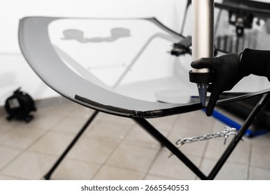 Applying adhesive to a car windshield using a caulking gun. Urethane caulking gun applies flexible adhesive, forming a watertight seal at car windshield replacement
