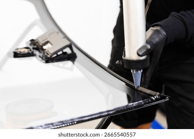 Applying adhesive to a car windshield using a caulking gun. Urethane caulking gun applies flexible adhesive, forming a watertight seal at car windshield replacement