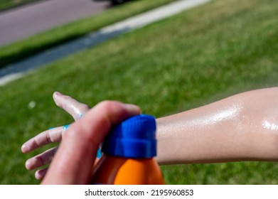 Applying An Aerosol Spray Sunscreen To A Young Child In The Summer. 