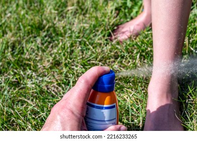 Applying An Aerosol Spray Sunscreen To A Young Child In The Summer. 