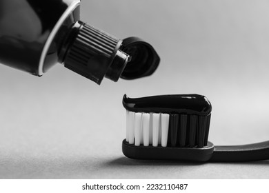 Applying charcoal toothpaste on brush against light grey background, closeup - Powered by Shutterstock