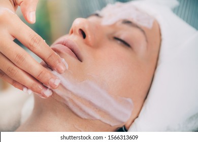 Applying face calming mask on beautiful woman’s face. Shaken protein mousse.