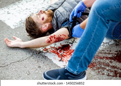 Applying first aid to the injured bleeding man, wearing tourniquet on the arm after the road accident on the pedestrian crossing