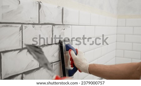 Applying grout to ceramic mosaic tiles. Working hands work with ceramic tiles. Working grouting of tiles, applying grout to the seam of tiles for home renovation in the kitchen.