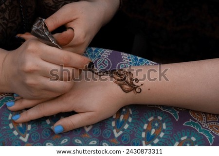 Applying henna feather design on hand, with colorful patterned fabric in the background
