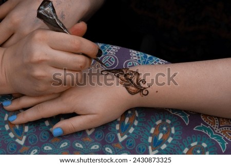 Applying henna feather design on hand, with colorful patterned fabric in the background