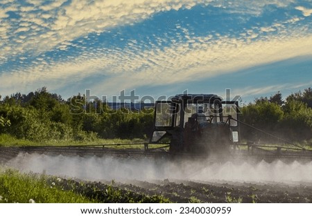 Applying herbicides to crops by spraying them with tractor-mounted sprayer.