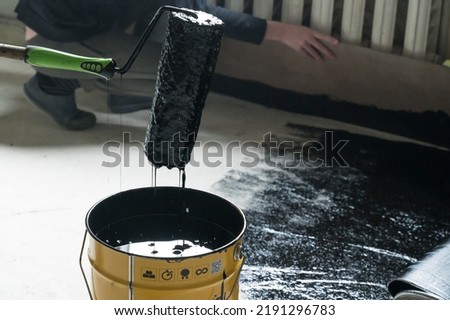 Applying hot resin to the floor for waterproofing, roller and bucket of resin, black and liquid resin.