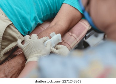Applying medical tape to secure clean dressing to a disinfected dog bite wound on the forearm of a patient at a bite center or local clinic.