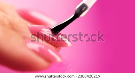 Applying Nail polish, pink shellac UV gel, varnish, nails manicure process concept in beauty salon. Transparent top coat drop on brush. Over pink background. Application of nail polish