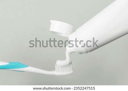 Applying paste on toothbrush against grey background