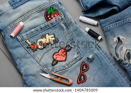 Applying patches to denim. Embroidered and sequin decorative elements to embellish worn jeans. DIY project concept.
