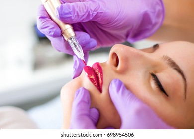 Applying permanent make up on lips of young girl with tattoo tool in beauty studio. Selective focus, close up - Shutterstock ID 698954506