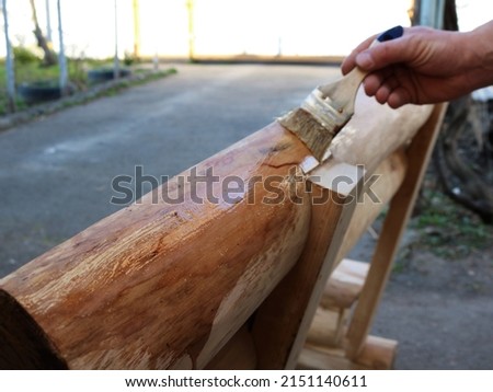 applying a protective clear varnish to the surface of a solid wood bench with a brush, varnishing outdoor country-style wooden furniture, varnishing a grained wood product