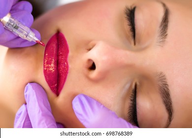 Applying red permanent make up tattoo on young girl lips