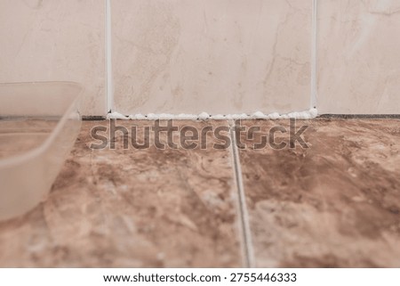 Applying sealant to the gap between ceramic tiles to prevent unsanitary conditions. Spreading white silicone along tile joint to seal gaps in bathroom wall and counter