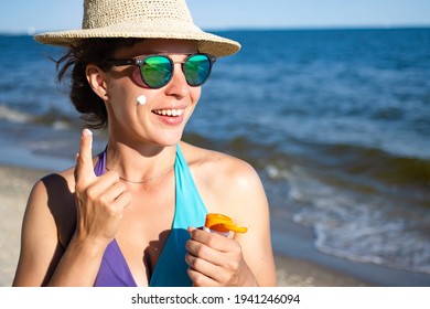 Applying sunscreen protection lotion spf. Young woman putting suntan solar cream to her cheek. Protection from burns, premature aging and skin cancer, dressed in blue swimsuit. Ocean in background