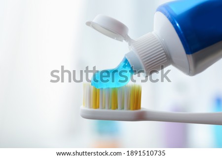 Applying toothpaste on brush against blurred background, closeup