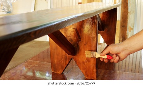 applying varnish on a wooden bench in a workshop, varnishing a wooden product by hand, manual lacquering of handmade furniture, processing with a protective varnish a bench made of wood