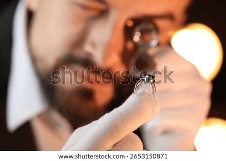 Appraiser with loupe evaluating luxury ring indoors, selective focus