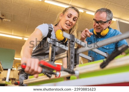 Apprentice and instructor working with clamps and wood in a bright workshop