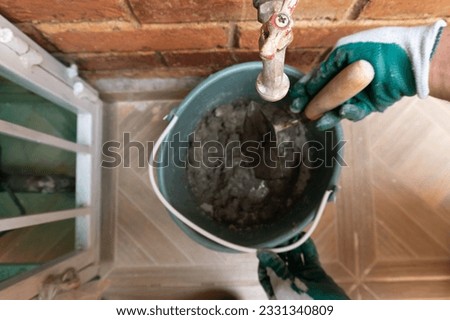 approach to a container full of cement mixture found with a blurred background, used to carry out masonry work. there are various objects in focus such as a metal key and the hands of a man