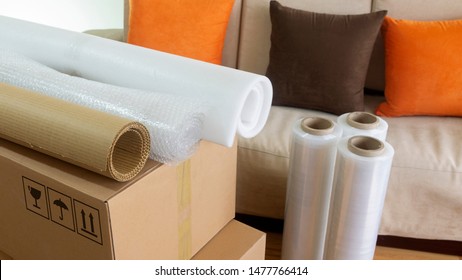 Approach to three rolls of cardboard, foam and bubble wrap used to pack things on a cardboard box with a sofa in the background