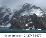    approaching the formidable mountain peaks, icebergs,  and glaciers of elephant island,  on the antarctic peninsula, on a  summer cruise on a  stormy day        