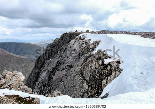 Approaching the\
summit of Ben Nevis, Scotland in June with snow still standing.\
Tiny figures encircle the summit\
cairn.