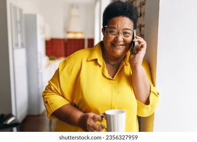 appy cheerful black senior plus size female with short haircut and eyeglasses having coffee break holding white cup while talking on phone with her friend, joking discussing funny situation - Powered by Shutterstock