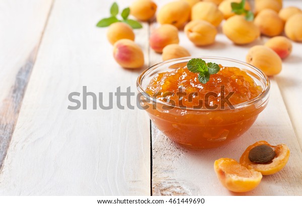 Apricot jam in a glass bowl, fresh apricots in\
a basket on a light wooden\
background