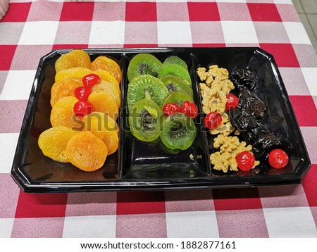 apricot, kiwi, cherry nuts and raisin in a black tray on a crossered red and withe tablecloth