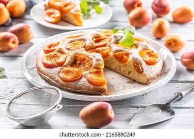 Apricot pie on a white plate, apricots, mint and powdered sugar on the kitchen table. - Powered by Shutterstock
