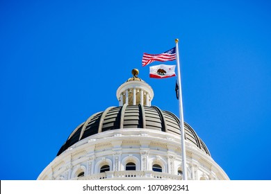 April 14, 2018 Sacramento / CA / USA - The US And The California State Flag Waving In The Wind In Front Of The Dome Of The California State Capitol