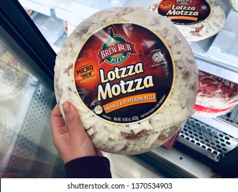 April 15, 2019 - Minneapolis, MN: Female Shopper Holds Up A Frozen Pizza - Lotzza Motzza Brew Pub Personal Pizza From A Grocery Store's Frozen Food Section