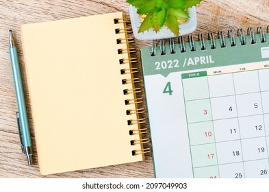 April 2022 Desk Calendar And Diary With Small Plant On Wooden Background.